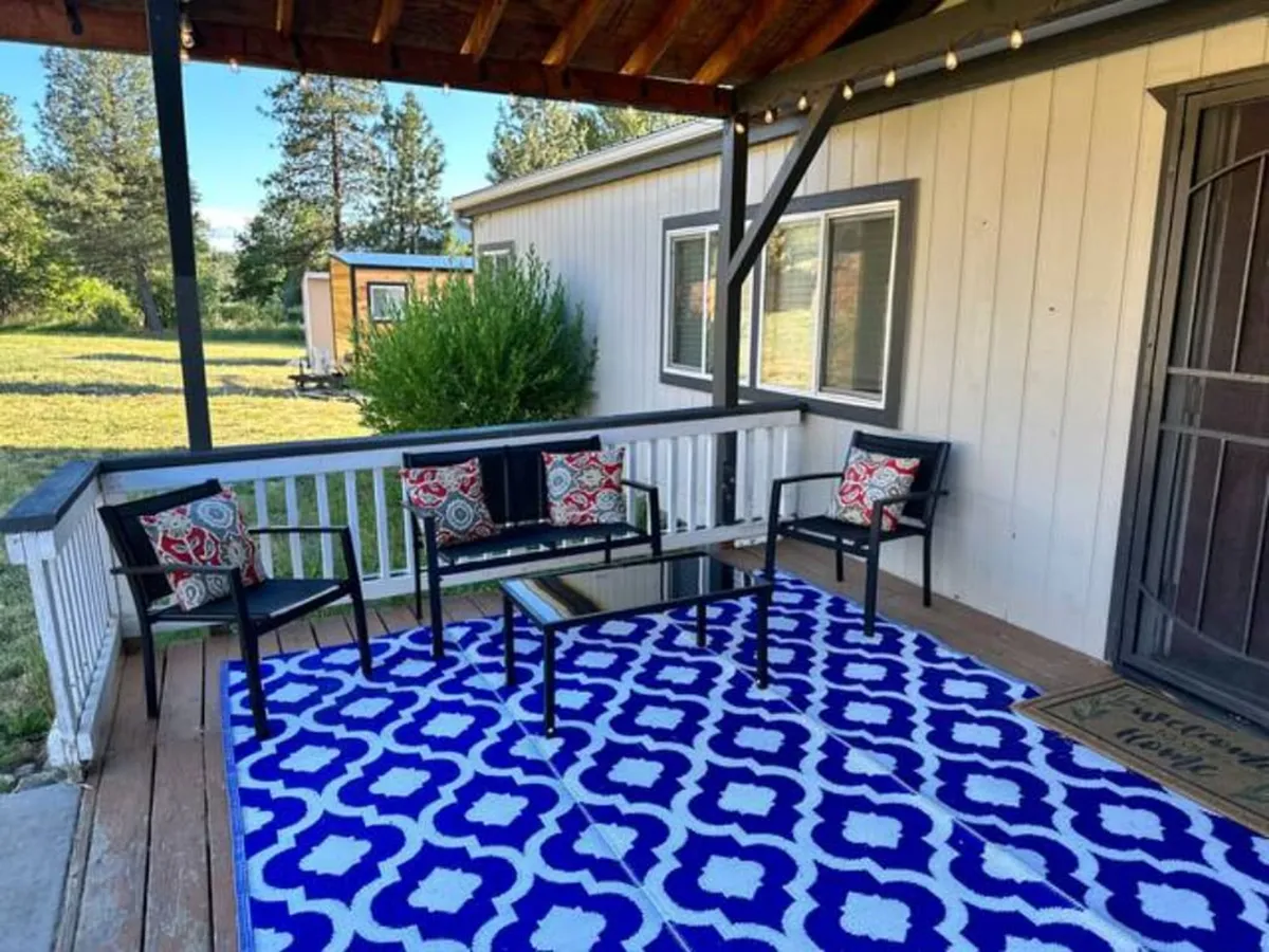 This image shows a welcoming wooden deck furnished with black chairs adorned with decorative cushions, a colorful rug beneath, and scenic views of the surrounding natural landscape. The setup encourages relaxation and connection with nature, suggesting a seamless transition between indoor comfort and outdoor adventure.