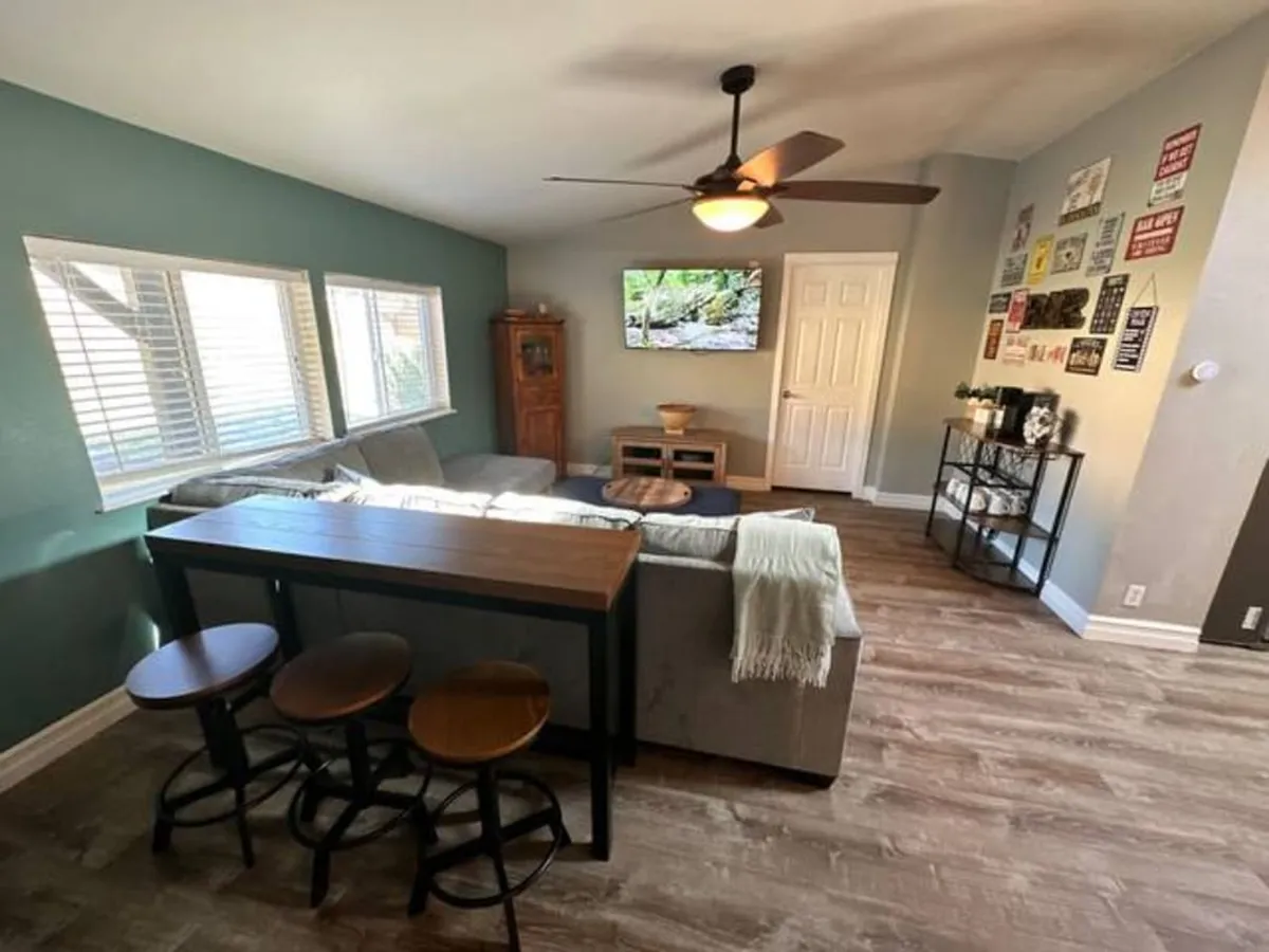 A view of a living space that includes a breakfast bar adjacent to a cozy sofa and TV, accented with decorative wall signs. The breakfast bar visually connects to the kitchen, suggesting a seamless flow between cooking, eating, and relaxing.