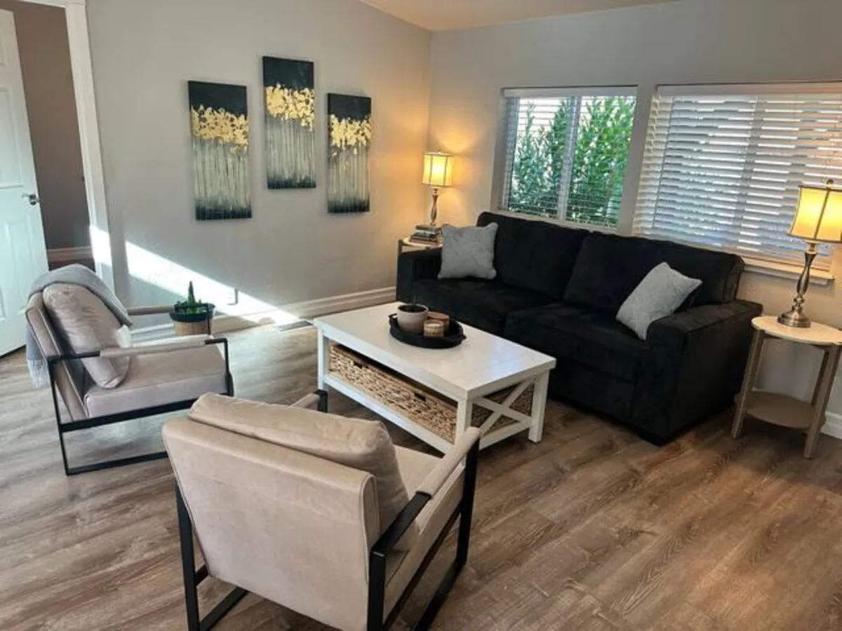 A cozy interior living room featuring a comfortable sofa, elegant artwork on the wall, a wooden coffee table, and ambient floor lamps. The space is arranged for intimate family gatherings and relaxation after a day outside.