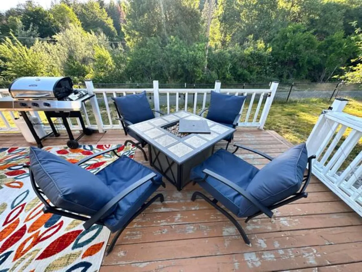 An inviting exterior space featuring a cozy outdoor seating area, a fire pit table, and a grill. The scene is set for social gatherings, relaxation, and enjoying the outdoors—perhaps while watching paragliders launch nearby.